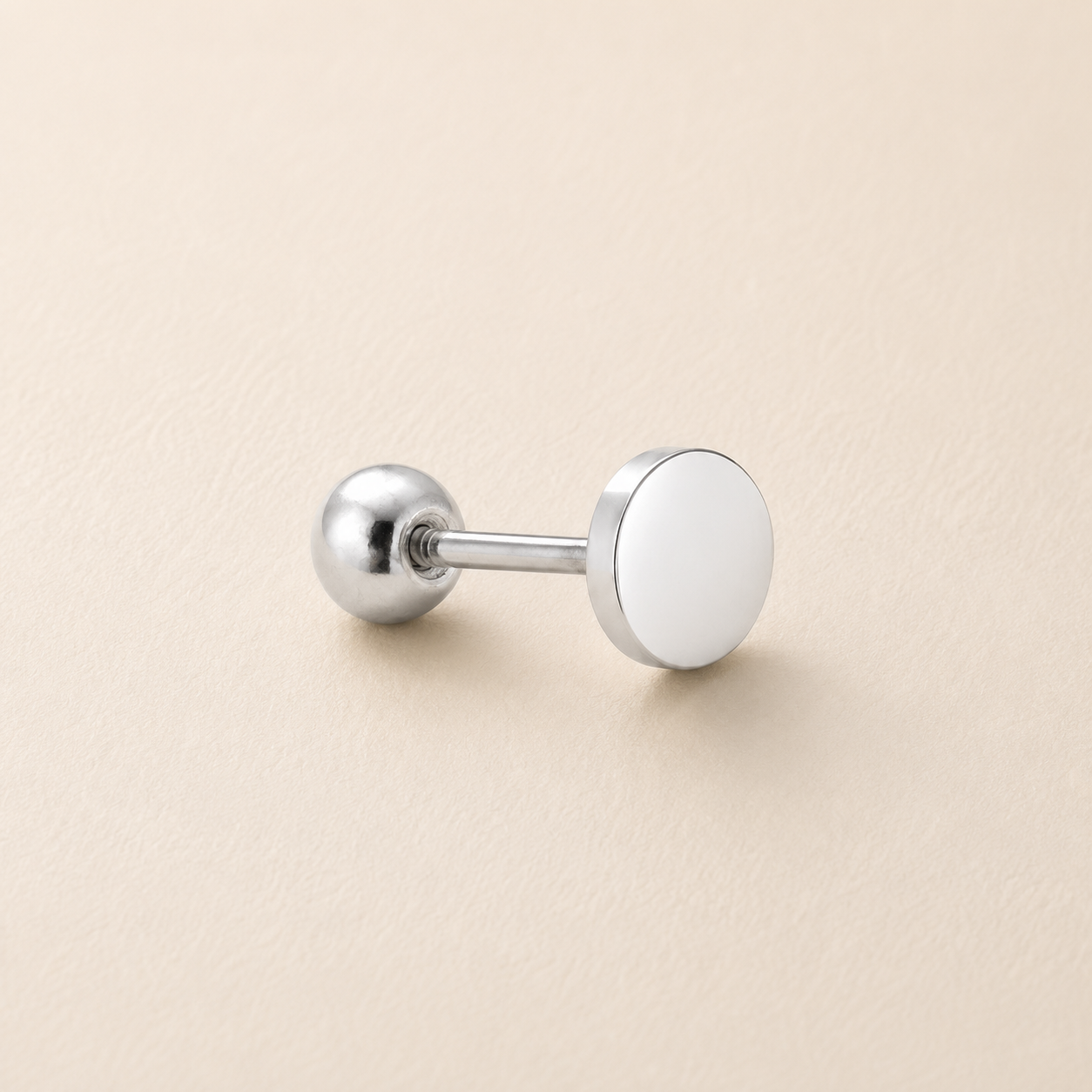A silver-toned labret stud earring with a flat circular disc face, shown on a light beige textured background.