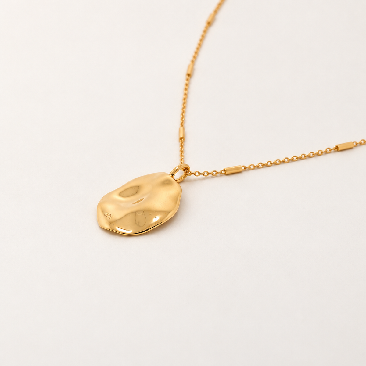 A gold necklace featuring a polished, organic-shaped pendant on a delicate gold chain, photographed on a clean white background.