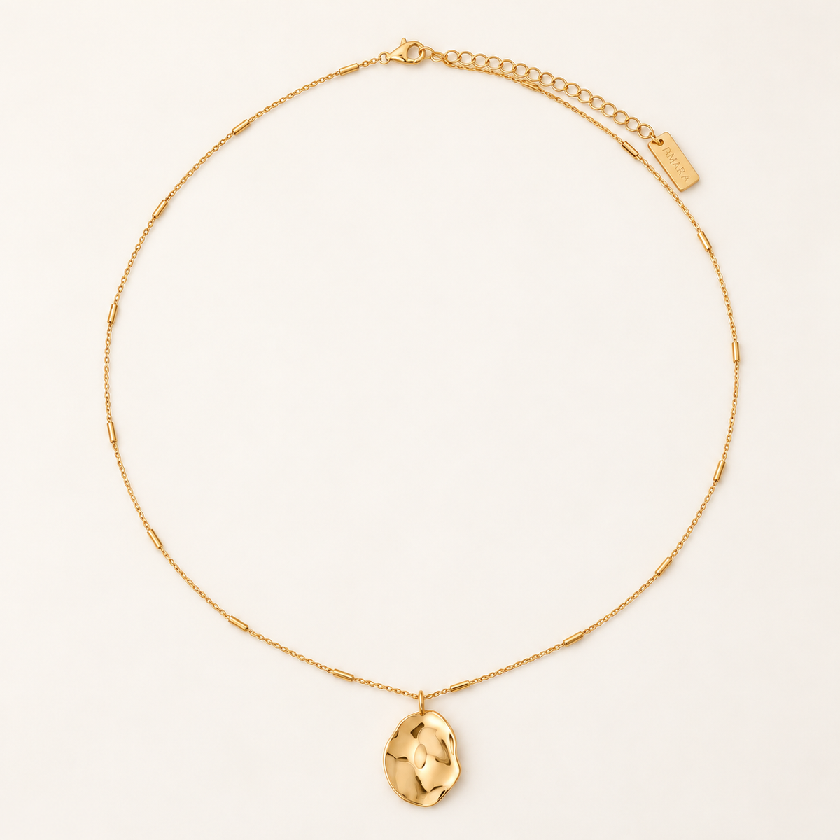 A delicate gold chain necklace featuring a small, textured, organic-shaped gold pendant, displayed on a clean off-white background.