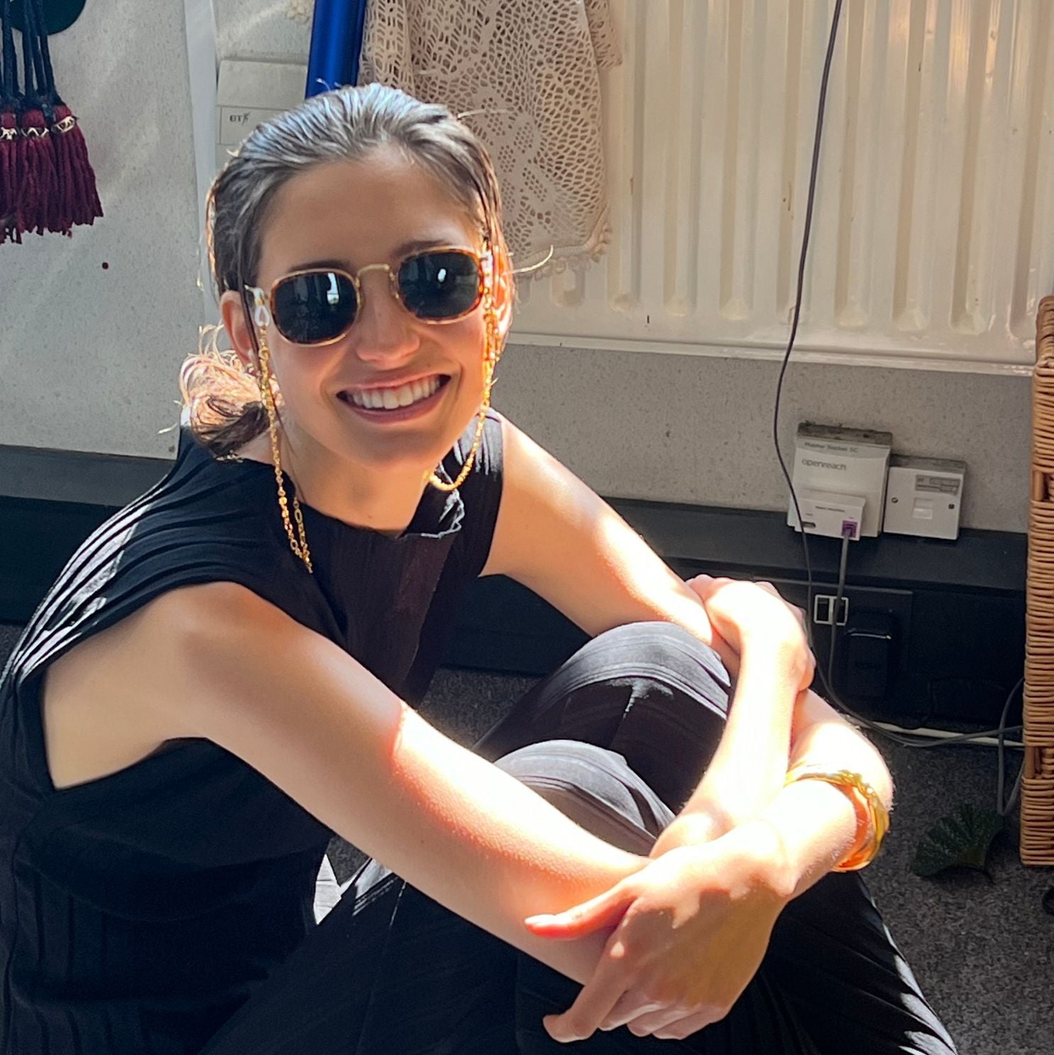 Woman wearing sunglasses and a black sleeveless top, sitting on the ground.
