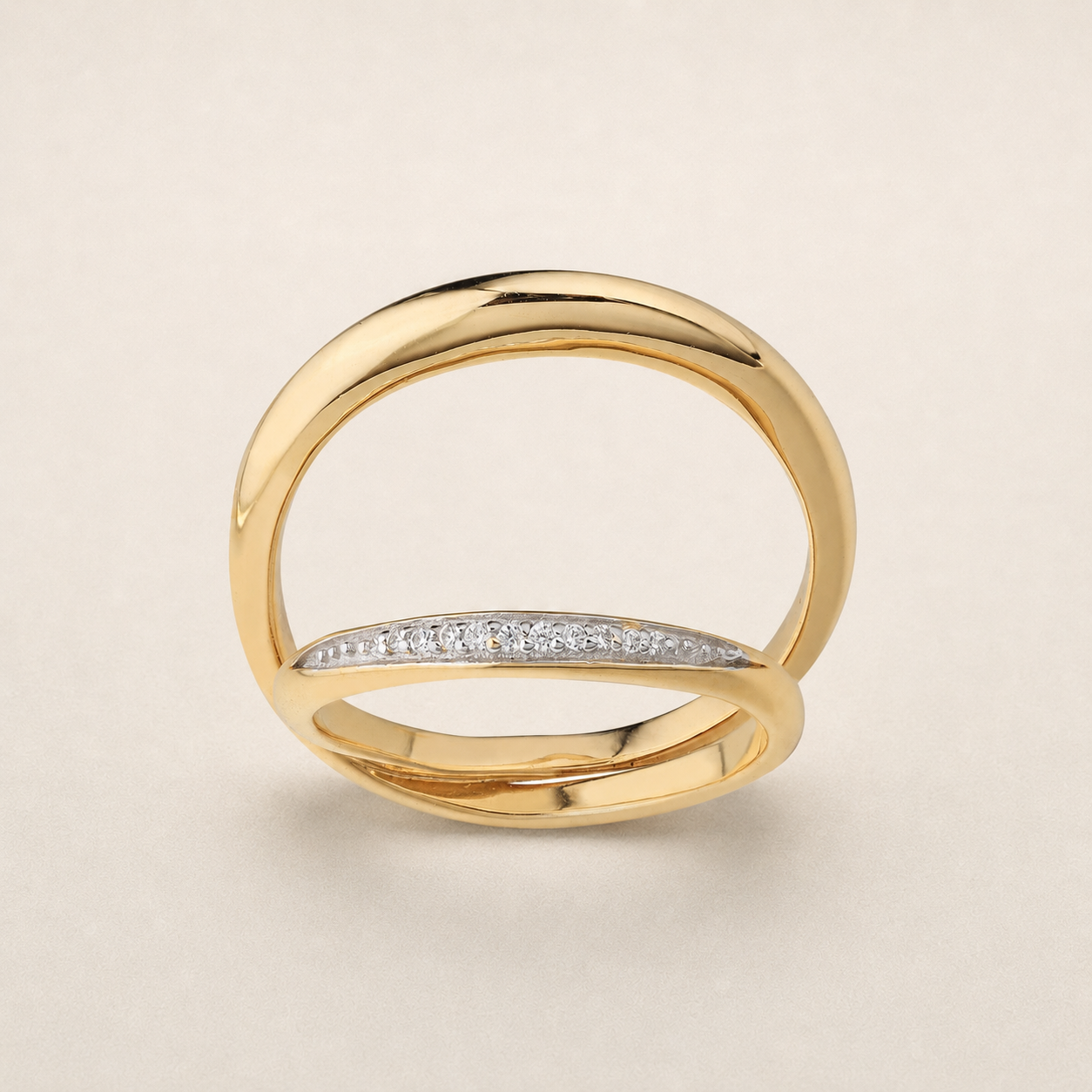A gold ring with a polished, open double-band design and a curved row of small clear stones across the front, set against a light beige background.