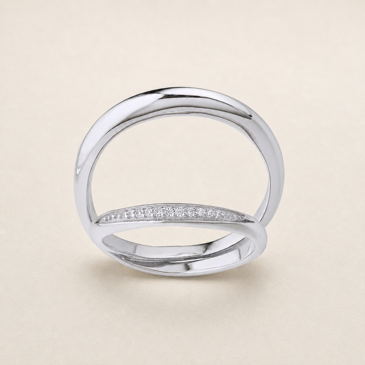 A polished silver-tone ring with a single row of small clear stones across the front, photographed on a plain warm beige background.