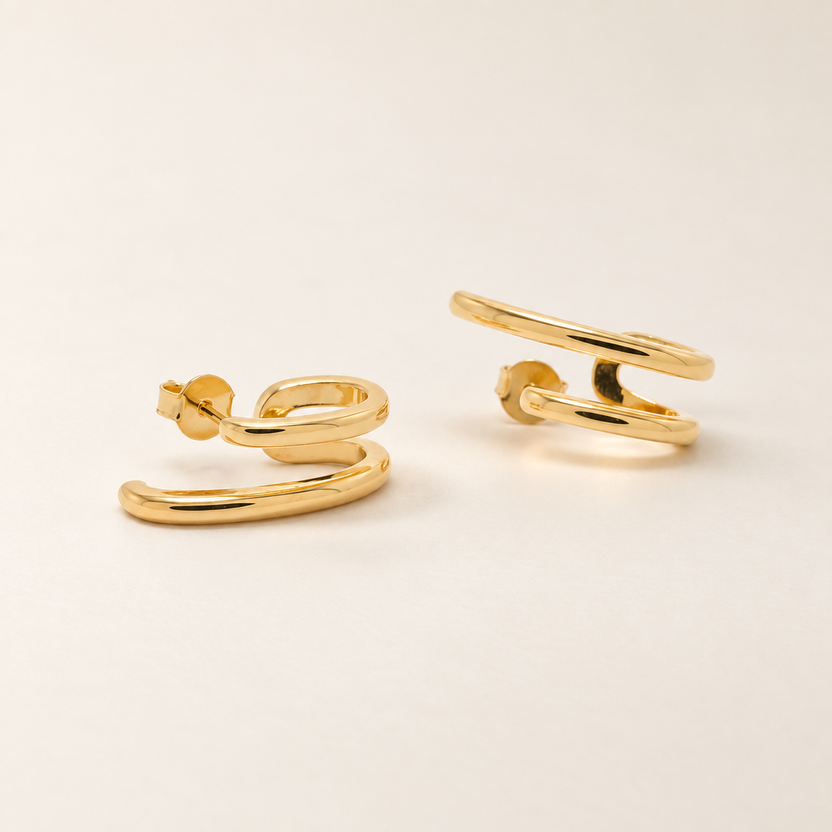 A pair of gold huggie hoop earrings with a polished, rounded organic design, displayed on a clean off-white background.