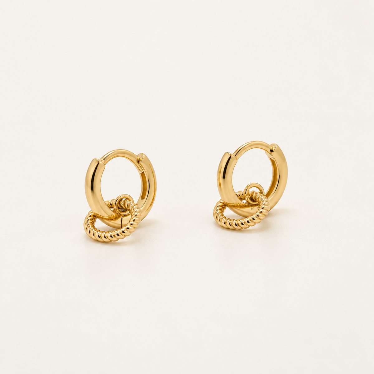 A pair of gold hoop earrings with a twisted rope detail, displayed on a clean, light off-white background.