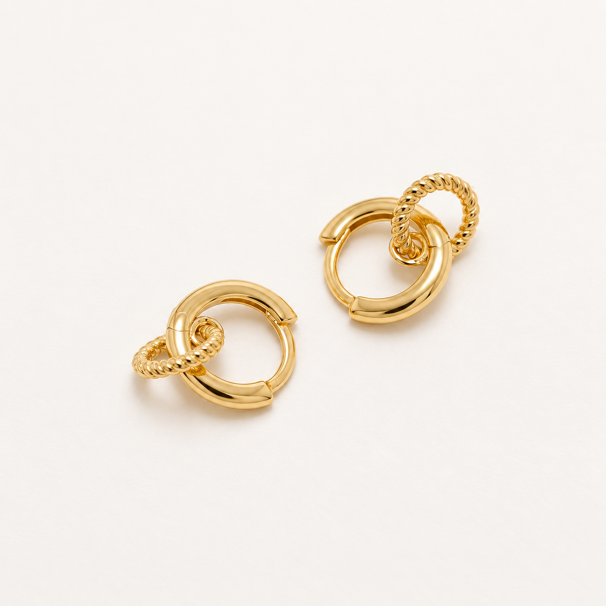 A pair of gold huggie hoop earrings with textured rope-style links, displayed on a clean off-white background.