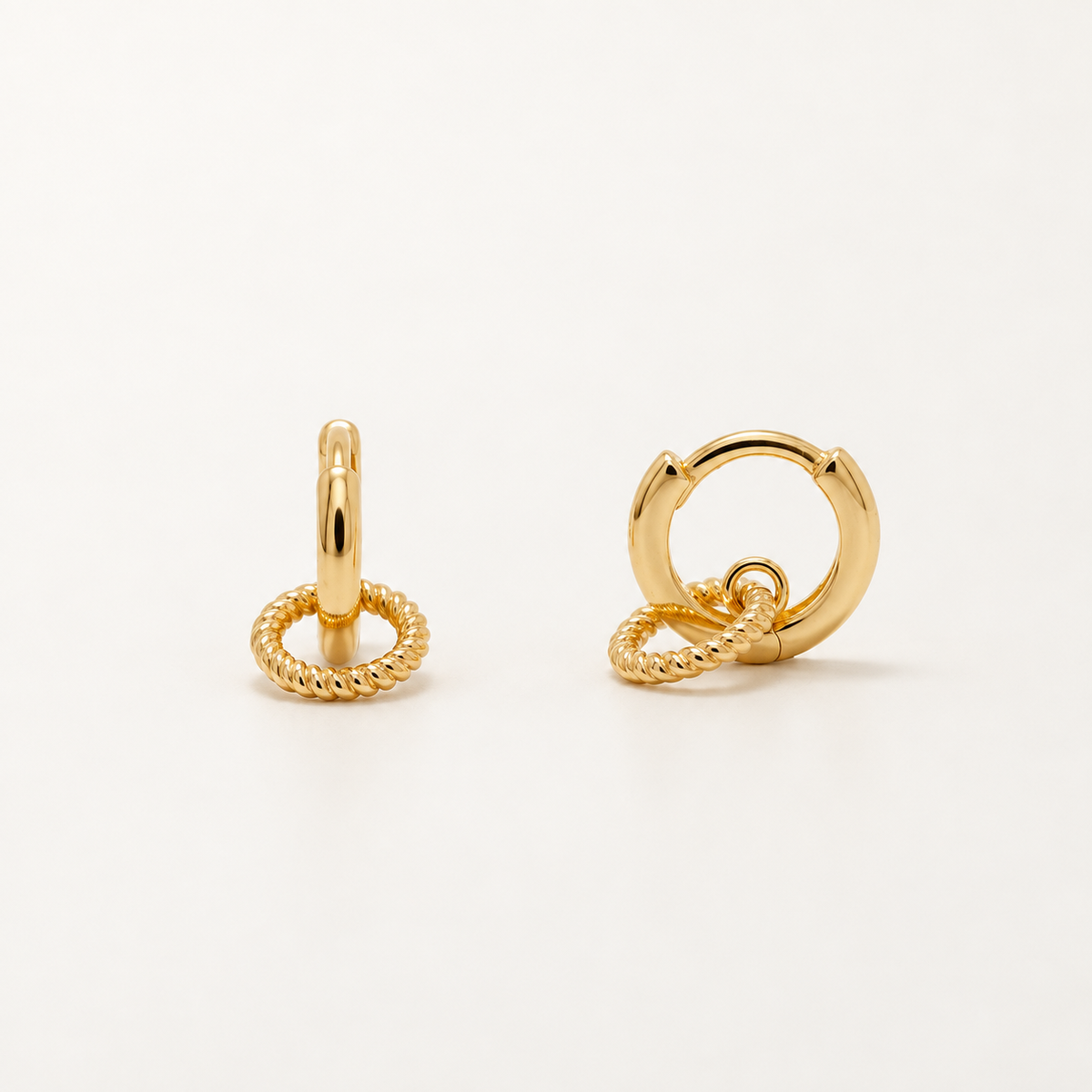 A pair of gold huggie hoop earrings with a twisted rope charm, shown on a clean white background.
