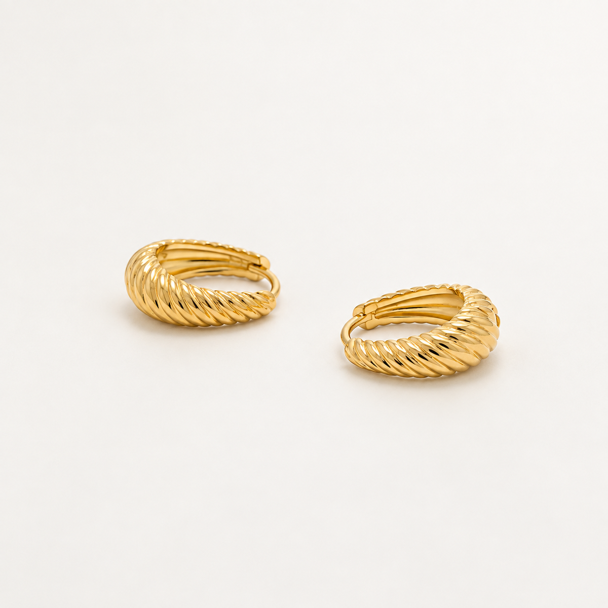A pair of gold huggie hoop earrings with a textured, twisted rope-like finish, displayed on a clean white background.