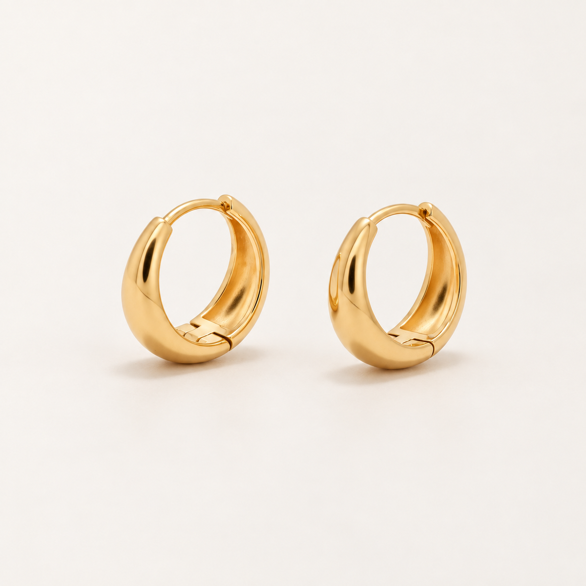 A pair of polished gold huggie hoop earrings on a clean, light off-white background.