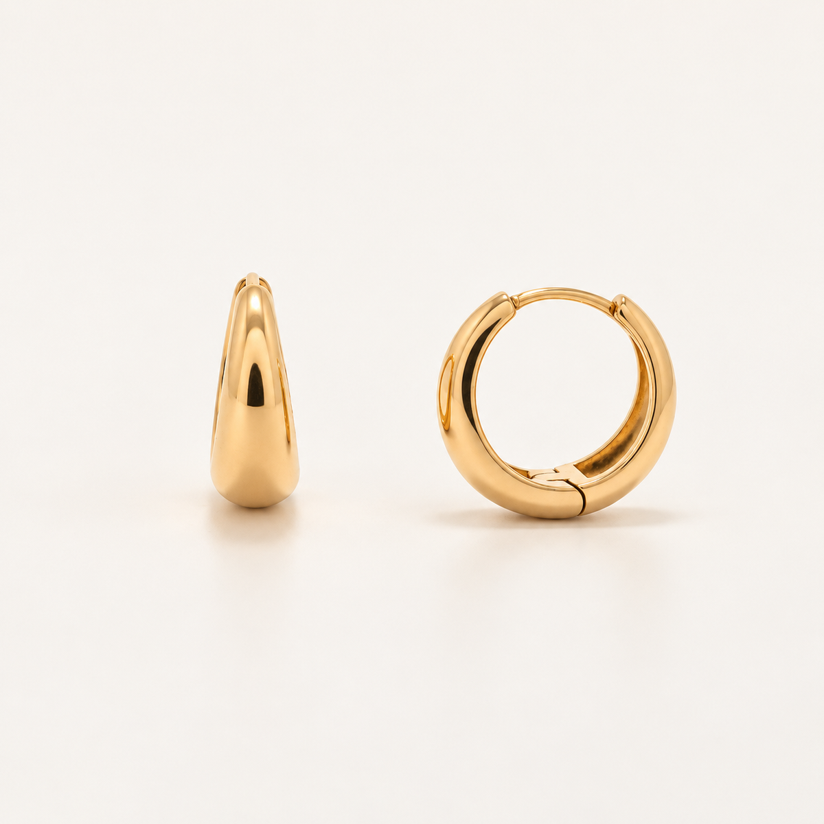 A pair of polished gold huggie hoop earrings, one shown from a side profile view and the other from a front-facing three-quarter view, set against a clean off-white background.