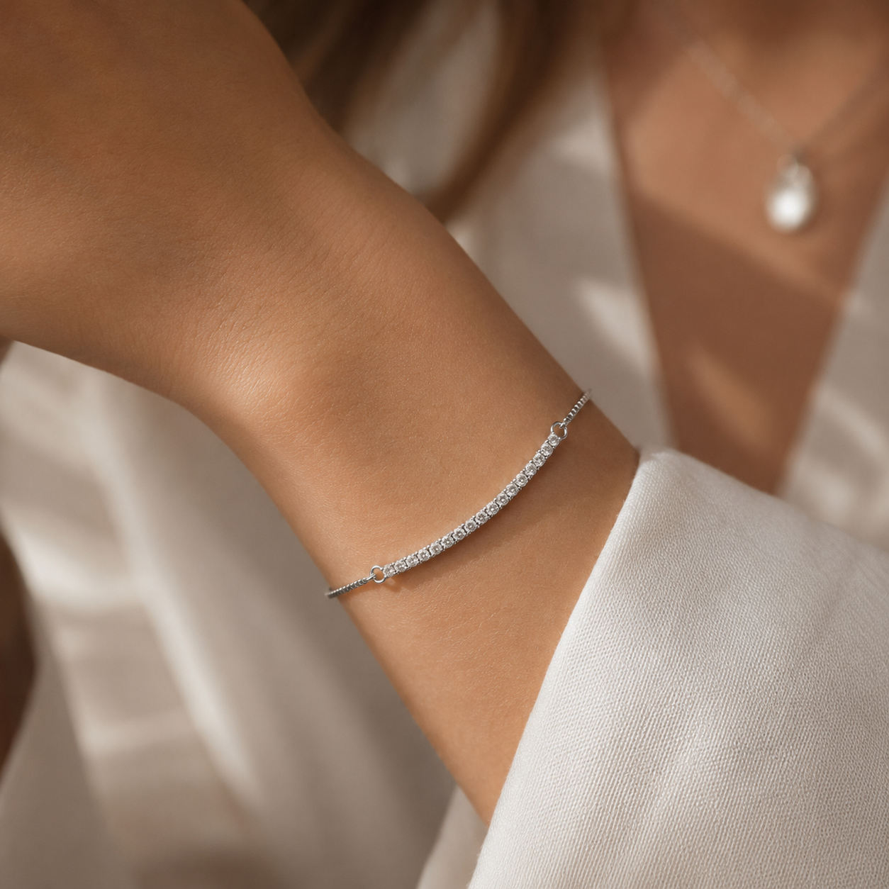 A delicate silver tennis bracelet with a pavé-set line of clear stones, shown worn on a woman's wrist. The bracelet features a small pavé diamond clasp.