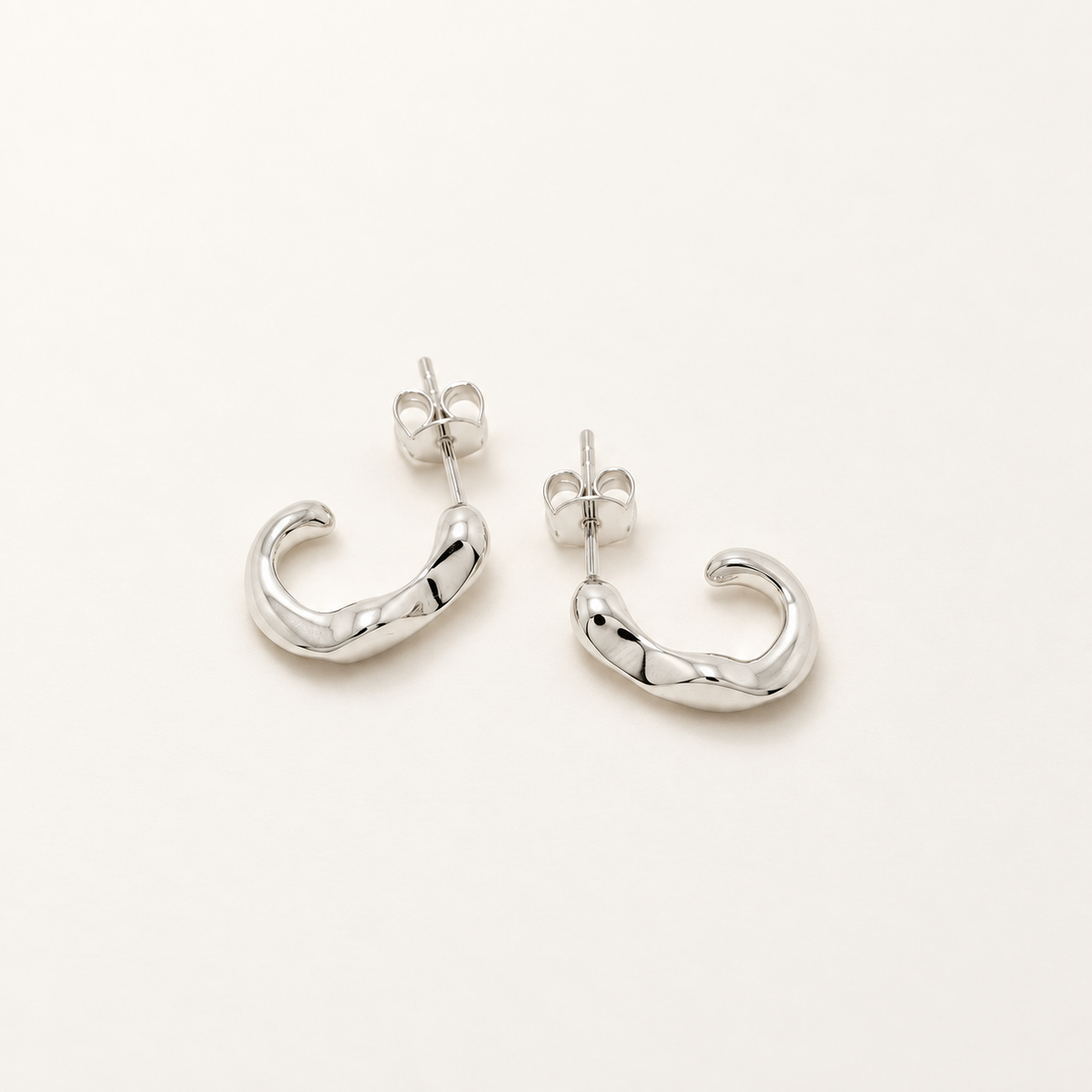 A pair of polished silver crescent-shaped hoop earrings with butterfly backings, displayed on a clean, light off-white background.