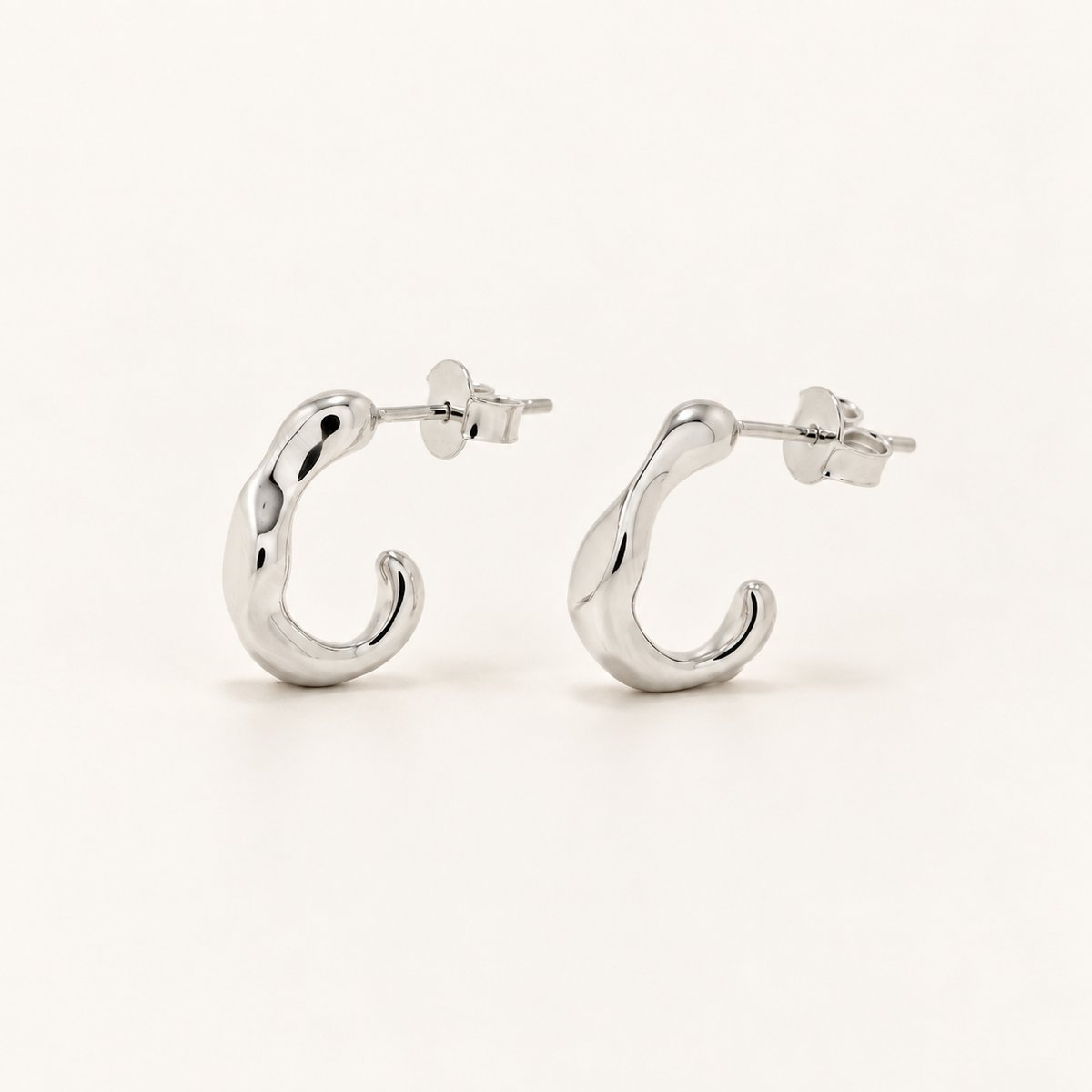 A pair of polished silver huggie hoop earrings with a twisted organic design, displayed on a clean off-white background.