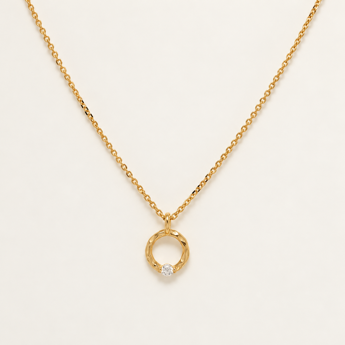 A delicate gold chain necklace with a small twisted circular pendant featuring a single clear gemstone, displayed on a clean off-white background.
