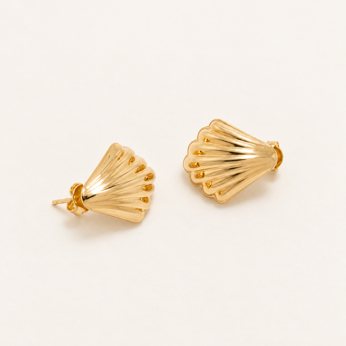 A pair of gold stud earrings with a textured, ribbed scalloped fan design, displayed on a clean off-white background.