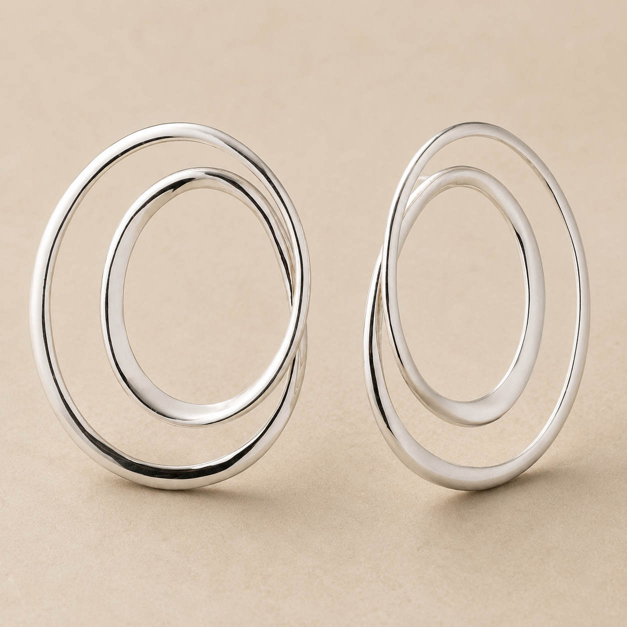 A pair of polished silver double-ring hoop earrings displayed on a neutral beige background.