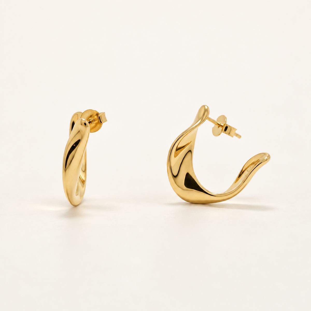 A pair of polished gold huggie hoop earrings shown on a clean, light beige background. One earring is displayed from the front, showing its twisted loop design, while the other is shown from the side, displaying its post and butterfly back.