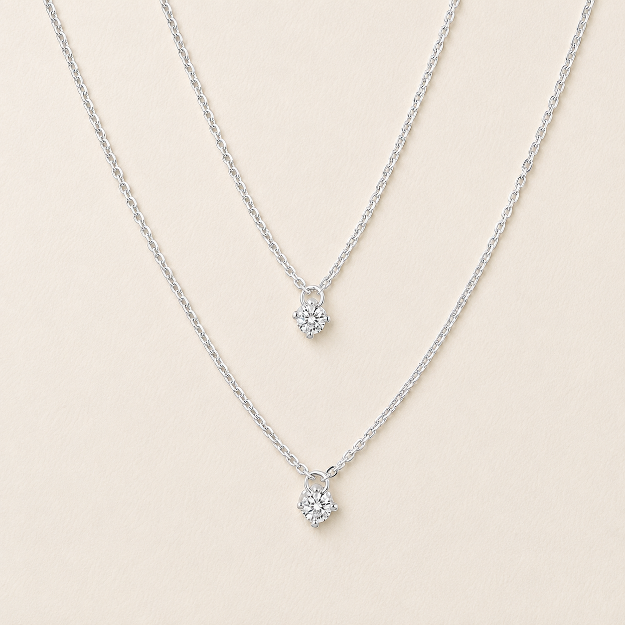 Two delicate silver chain necklaces with small floral cluster pendants, displayed on a light beige background.