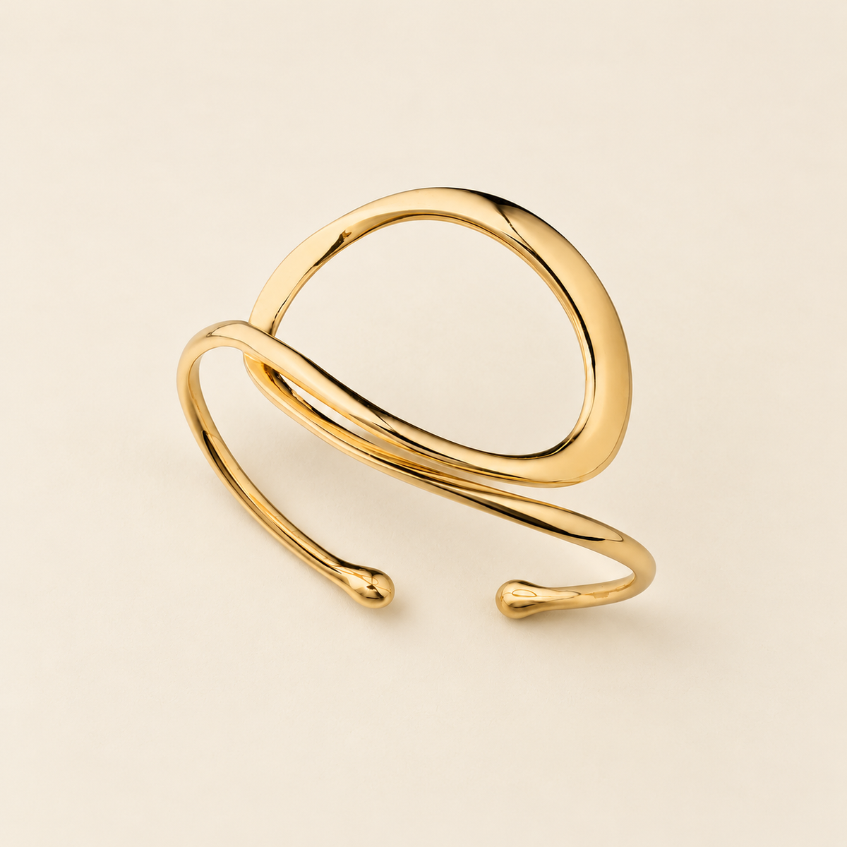 A polished gold open cuff bracelet with a modern, organic wavy design, photographed on a clean, solid light beige background.