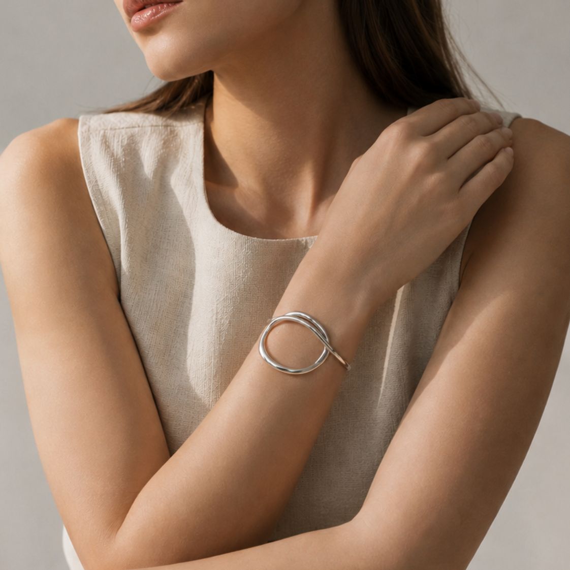 A woman wearing a minimalist silver circular open-bangle bracelet, posed in a neutral beige sleeveless top against a soft beige background.
