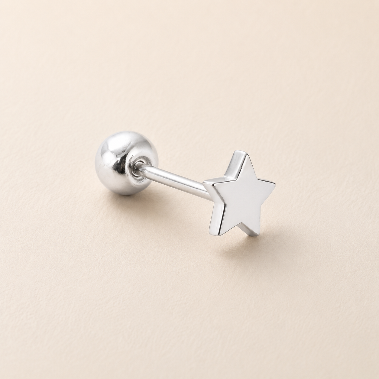 A silver-toned labret piercing stud with a star-shaped front and a spherical ball back, shown on a light beige textured background.