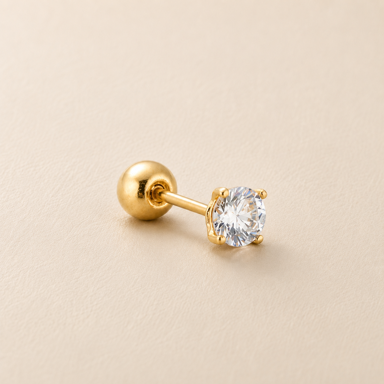 A single gold stud earring with a round brilliant-cut clear gemstone in a prong setting, shown on a textured beige background.