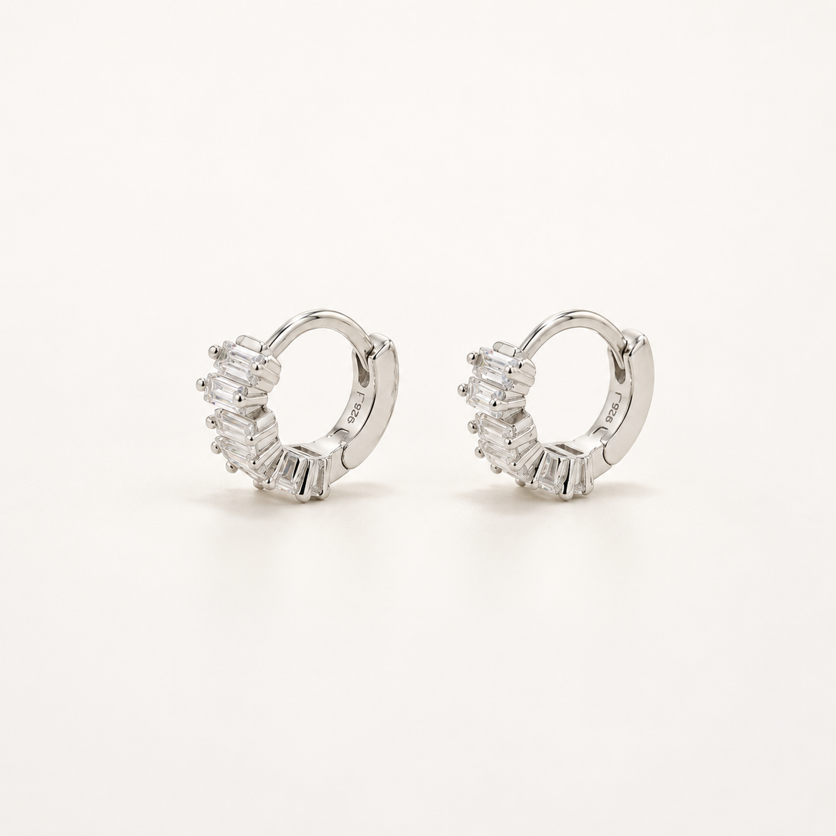 A pair of silver huggie hoop earrings adorned with baguette-cut clear stones, displayed on a clean white background.