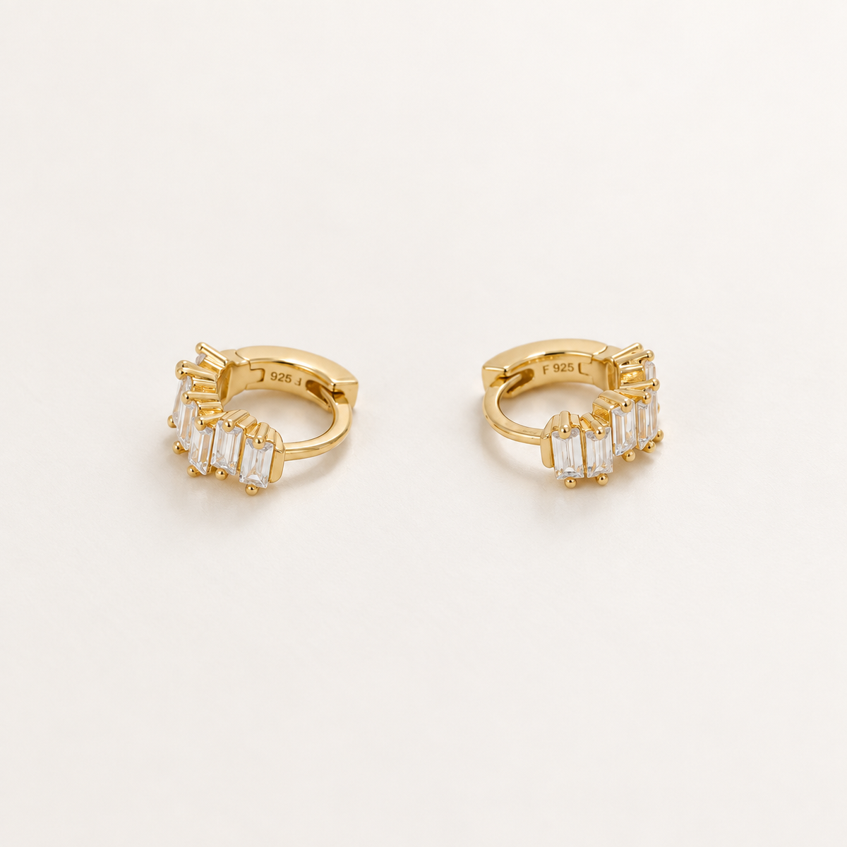 A pair of gold huggie hoop earrings with baguette-cut clear stones, shown on a clean white background. The inside of the hoops is stamped with '925' and 'S925'.