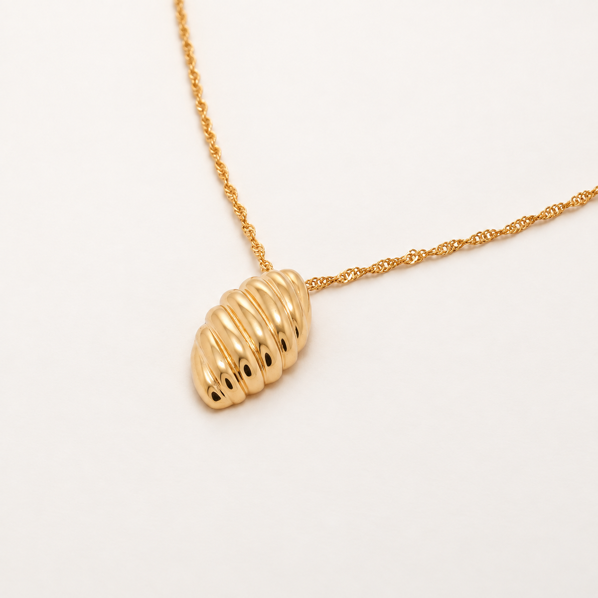 A gold chain necklace with a textured, ribbed oval pendant, photographed on a clean white background.