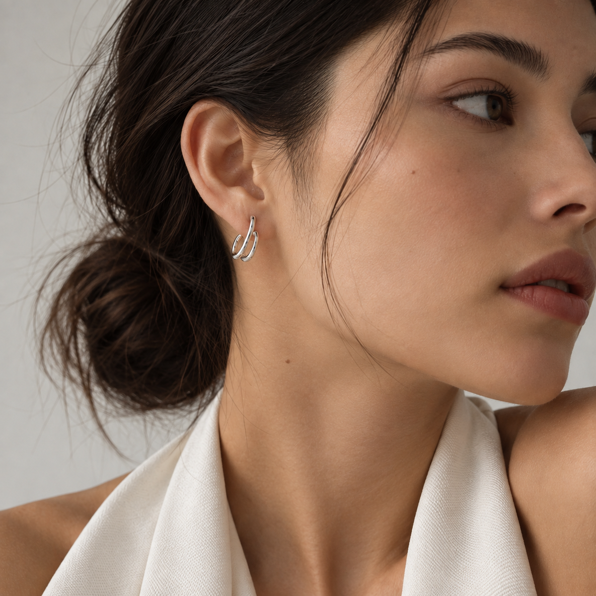 A close-up of a woman wearing a delicate silver hoop earring with a small clear gemstone, shown in profile against a soft light gray background.