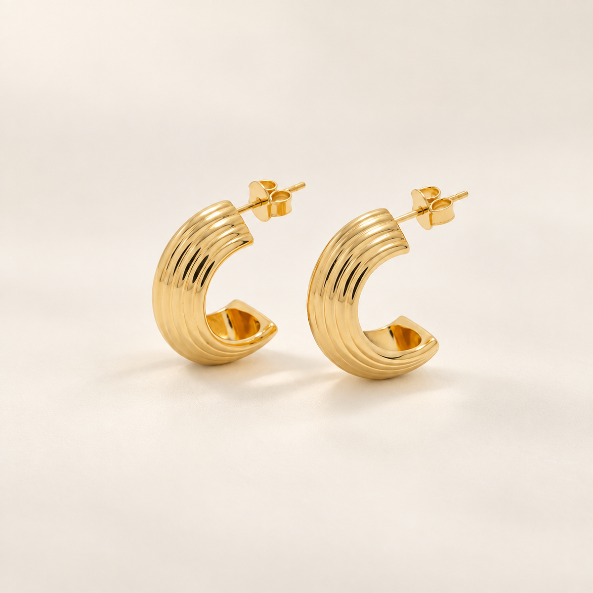 A pair of gold crescent-shaped hoop earrings with a ribbed, textured surface, displayed on a clean off-white background.