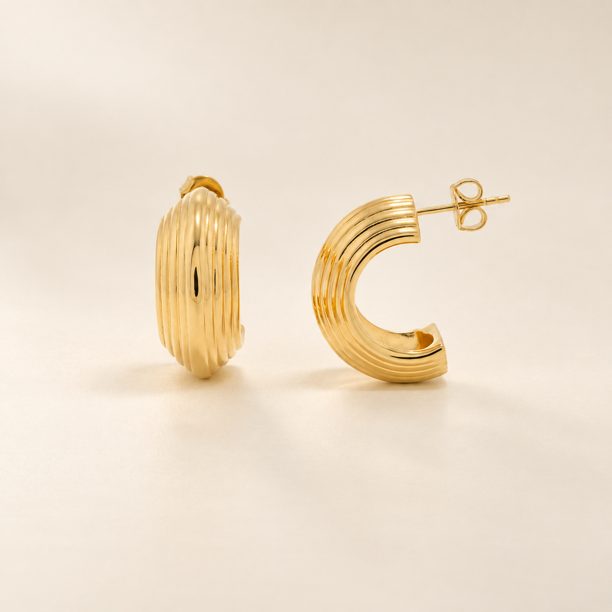 A pair of gold-toned hoop earrings with a ribbed, textured finish, shown on a clean, light beige background.