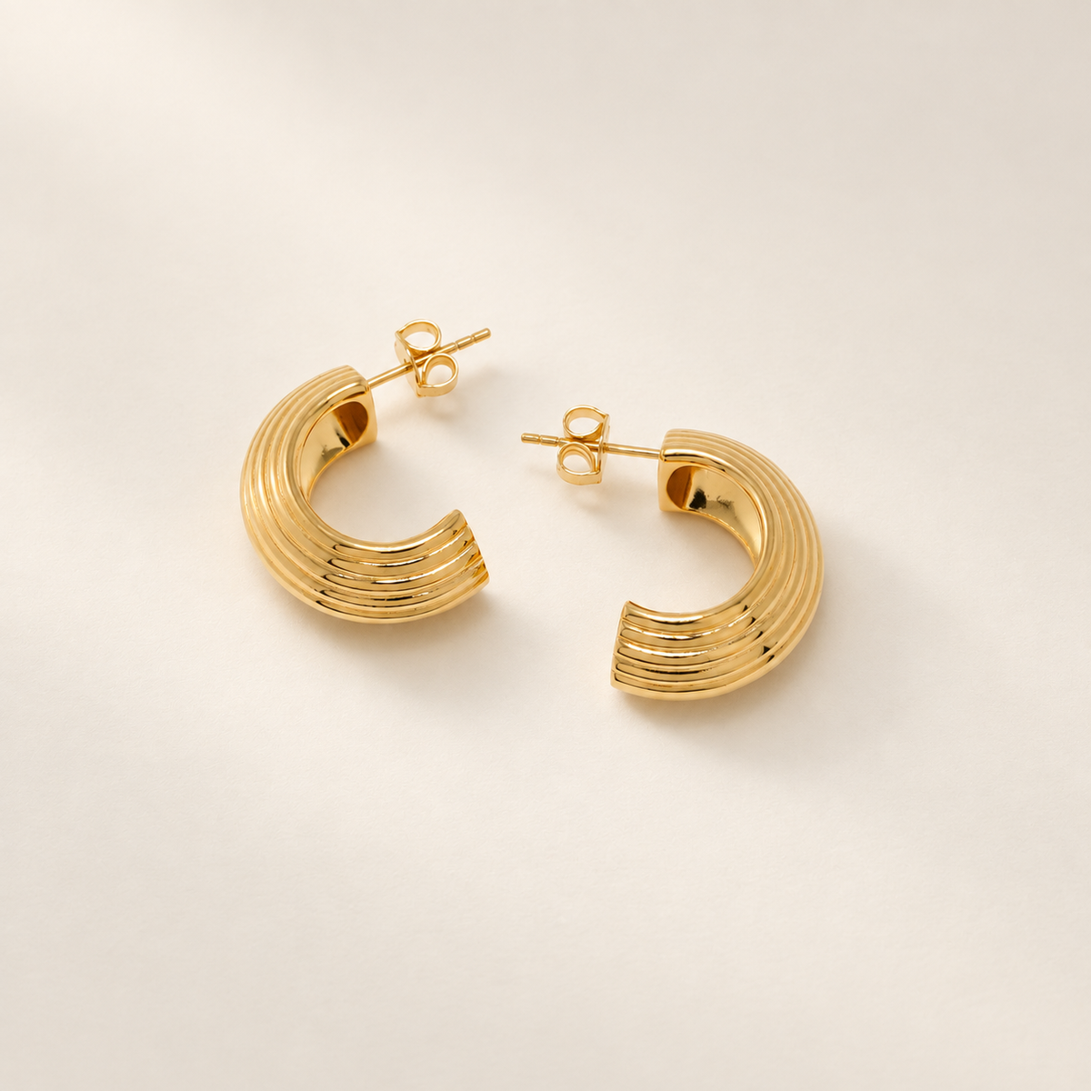 A pair of gold crescent-shaped hoop earrings with a textured, ridged surface, displayed on a clean, light beige background.