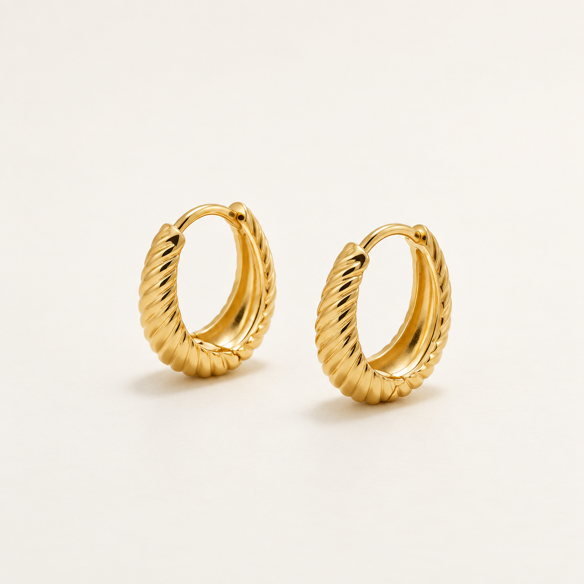 A pair of gold huggie hoop earrings with a textured, rope-like twisted design, displayed on a clean off-white background.