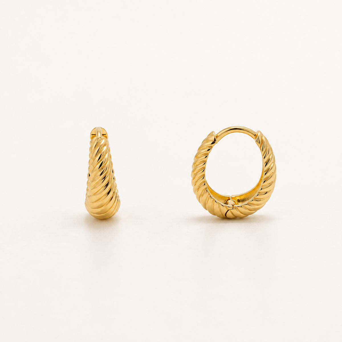 A pair of gold-toned twisted cable hoop earrings on a clean, off-white background. One earring is shown in profile, displaying its tapered shape and textured twisted design, while the other is shown from the front, displaying the hinged clasp.
