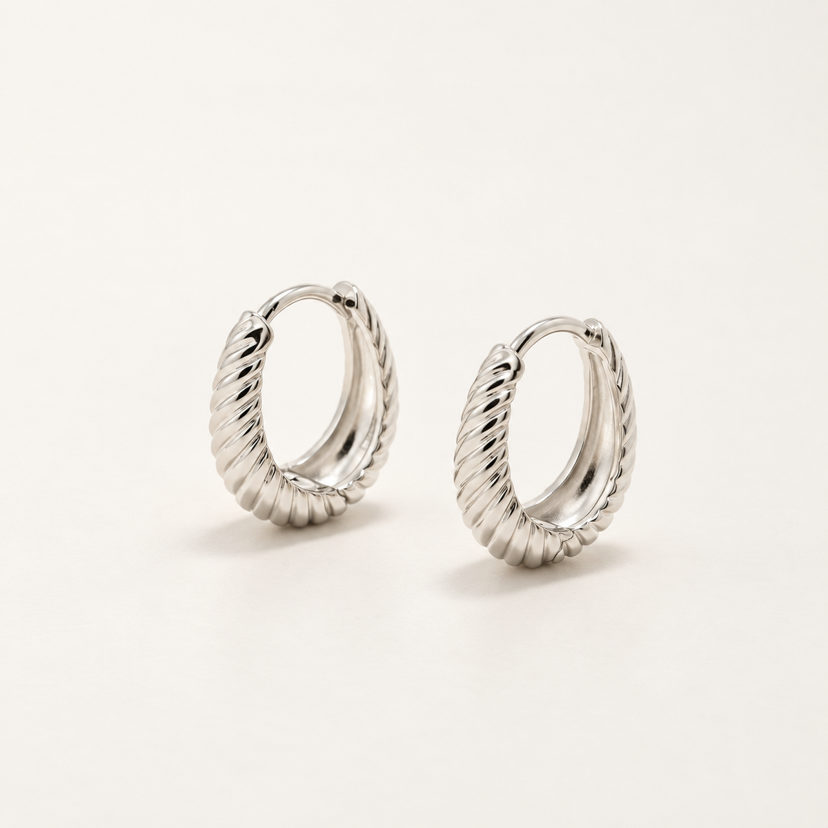 A pair of silver cable-knit hoop earrings on a clean, light off-white background.