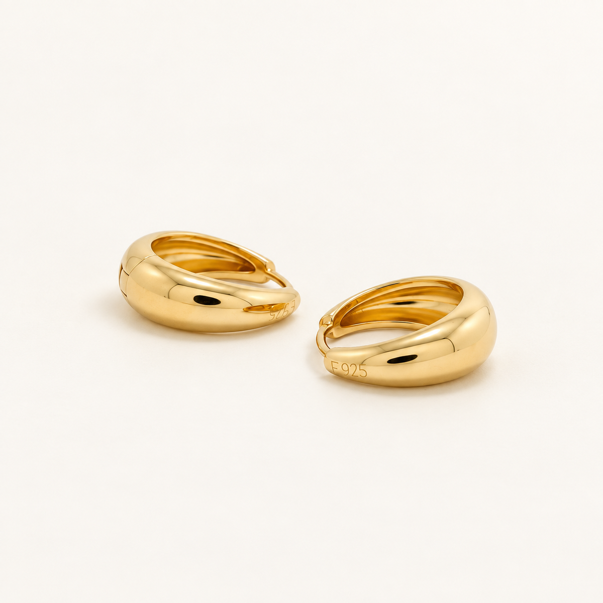 A pair of polished yellow gold huggie hoop earrings on a clean, off-white background.