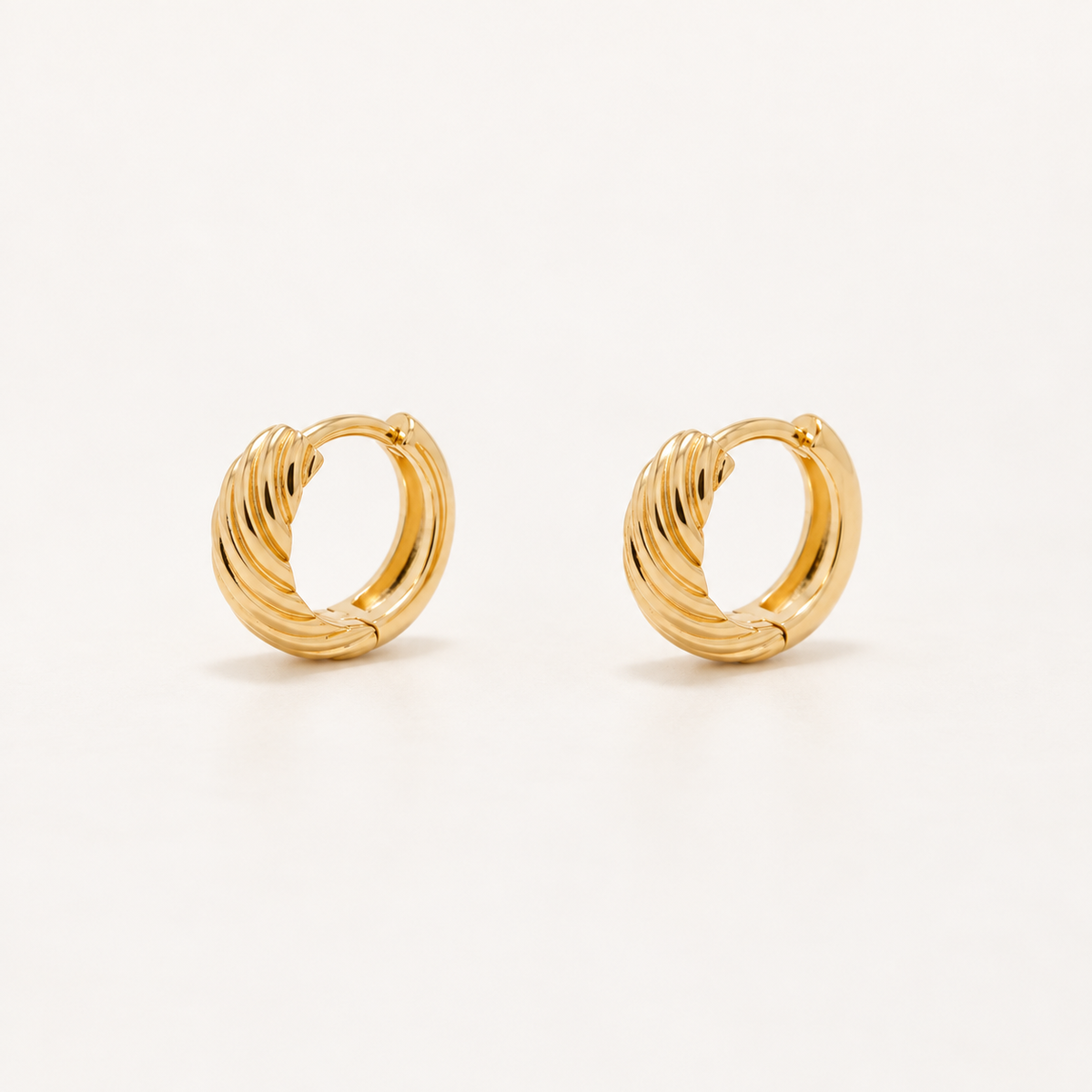 A pair of gold huggie hoop earrings with a textured, twisted ribbed design, displayed on a clean off-white background.