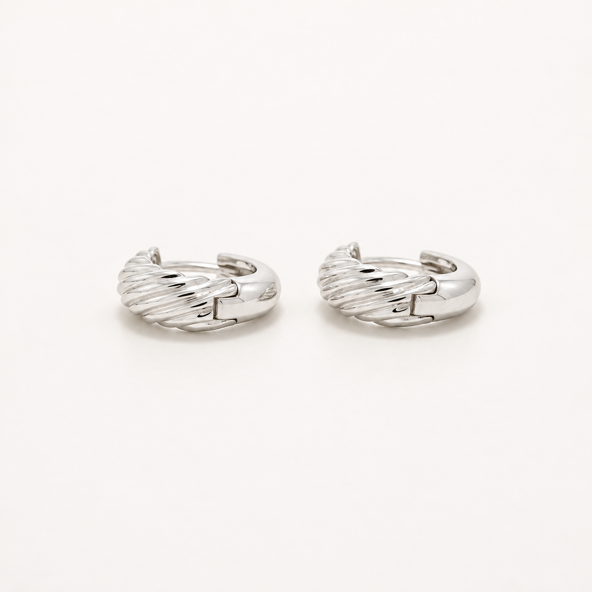A pair of silver huggie hoop earrings with a textured, twisted cable-like design, displayed on a clean white background.