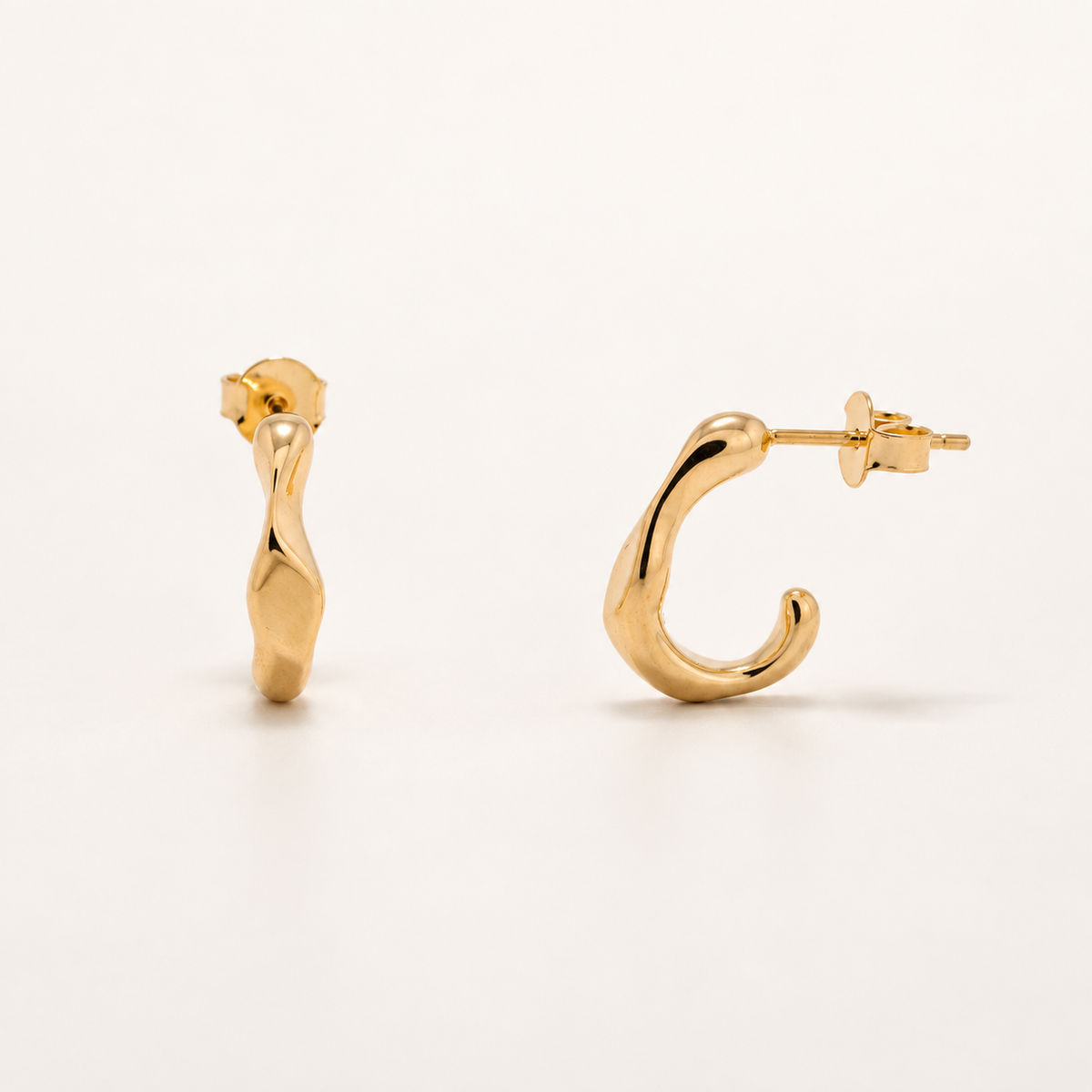 A pair of gold huggie hoop earrings with a polished, organic wavy texture, shown from two angles on a clean off-white background.