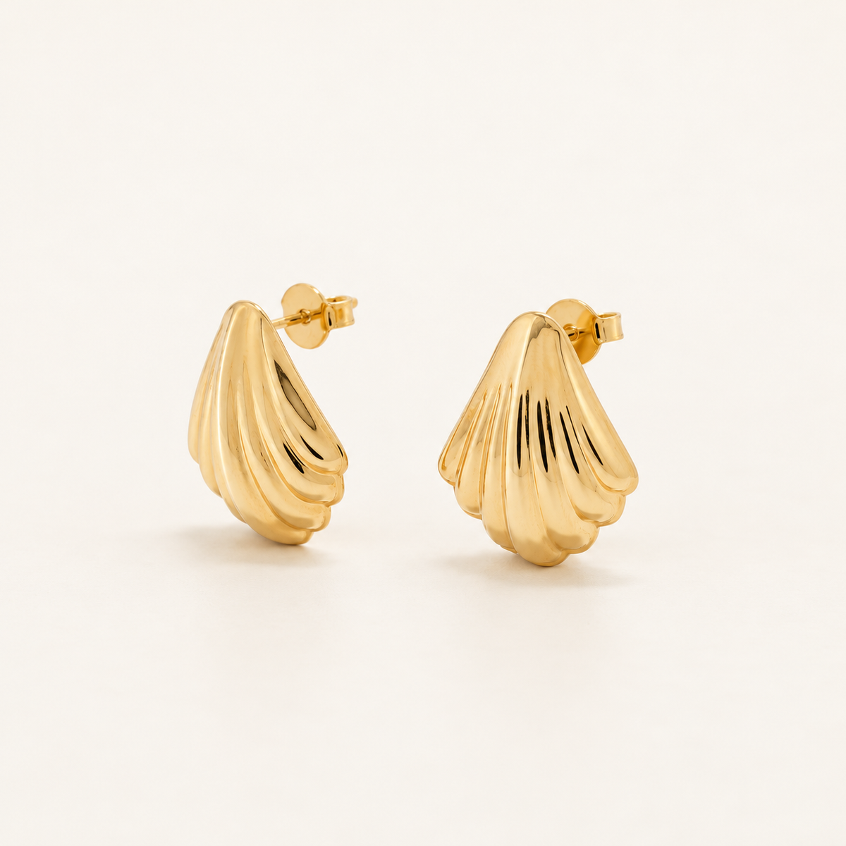 A pair of gold shell-shaped stud earrings with a ribbed, textured surface, shown on a clean off-white background.