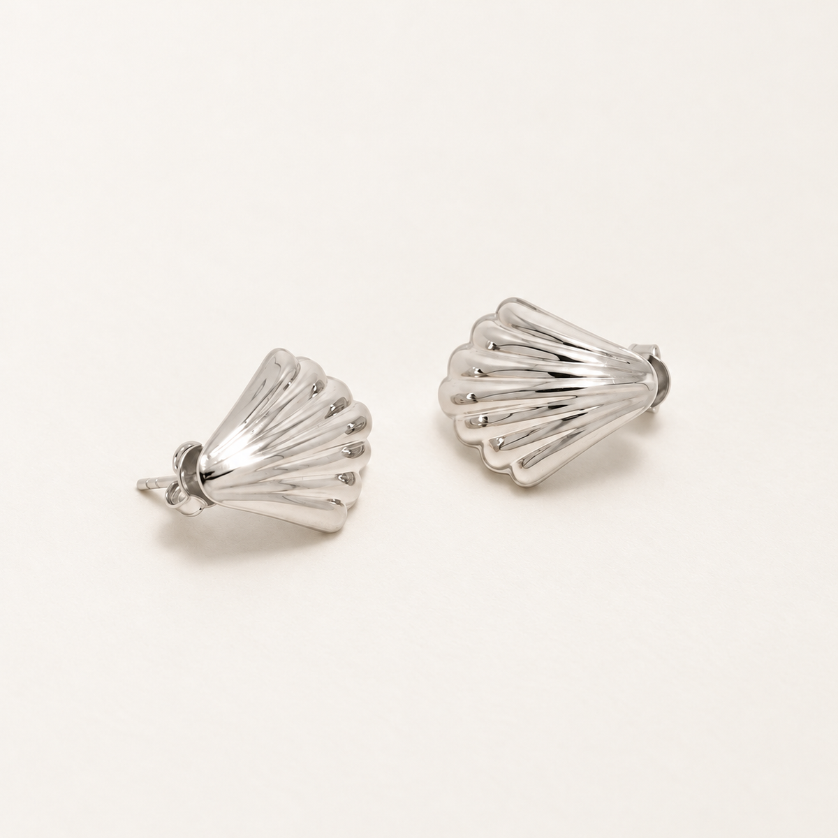 A pair of silver-toned shell-shaped stud earrings with a textured, ribbed exterior, displayed on a clean off-white background.
