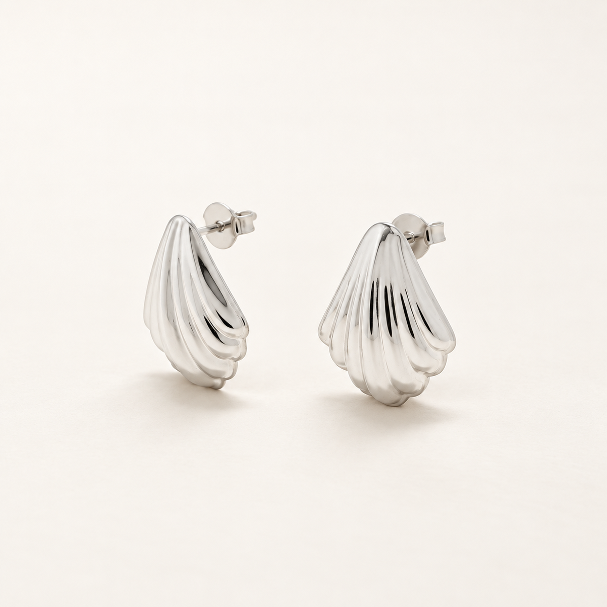 A pair of polished silver shell-shaped stud earrings with a ribbed, textured surface, displayed on a clean off-white background.
