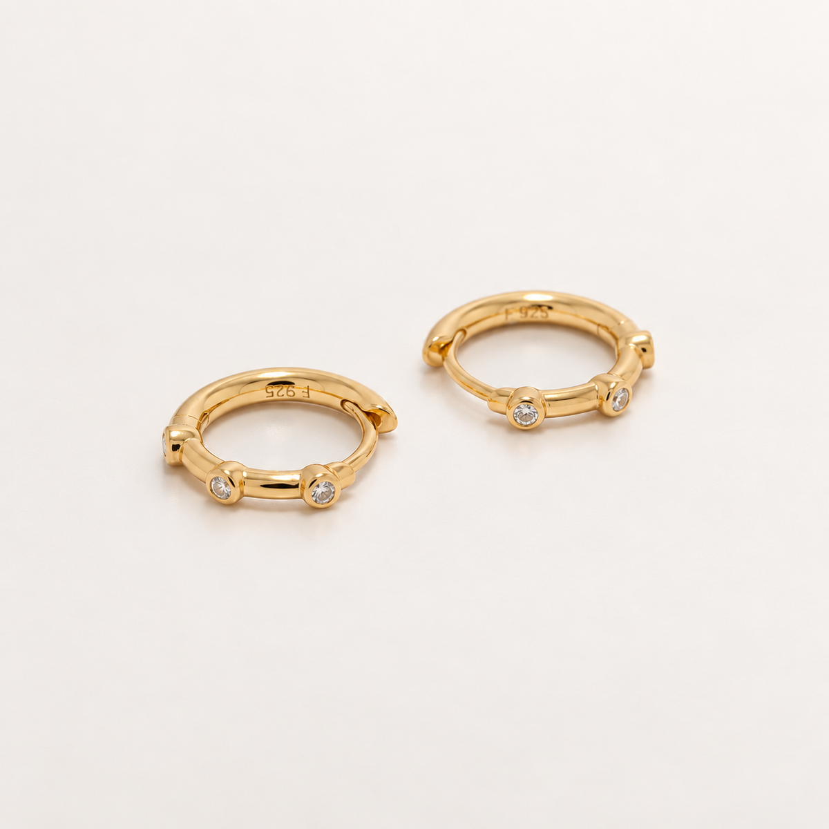 A pair of gold huggie hoop earrings with small clear gemstones set along the front, photographed on a clean white background.