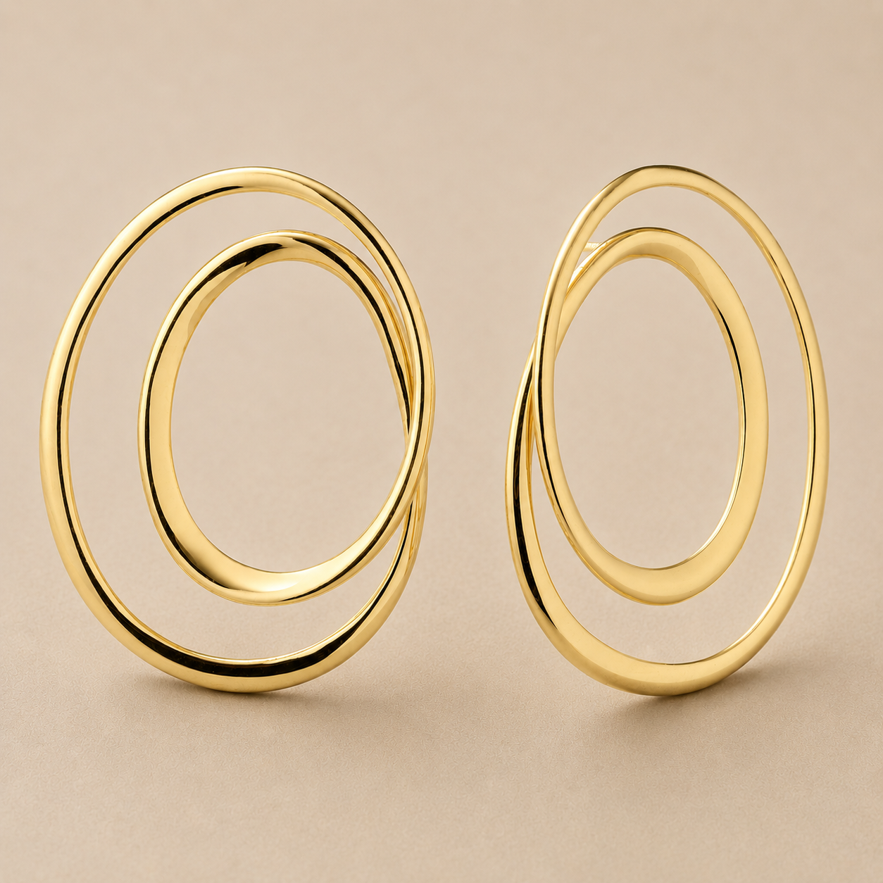 A pair of gold-toned double-ring hoop earrings with a polished finish, displayed on a neutral beige background.