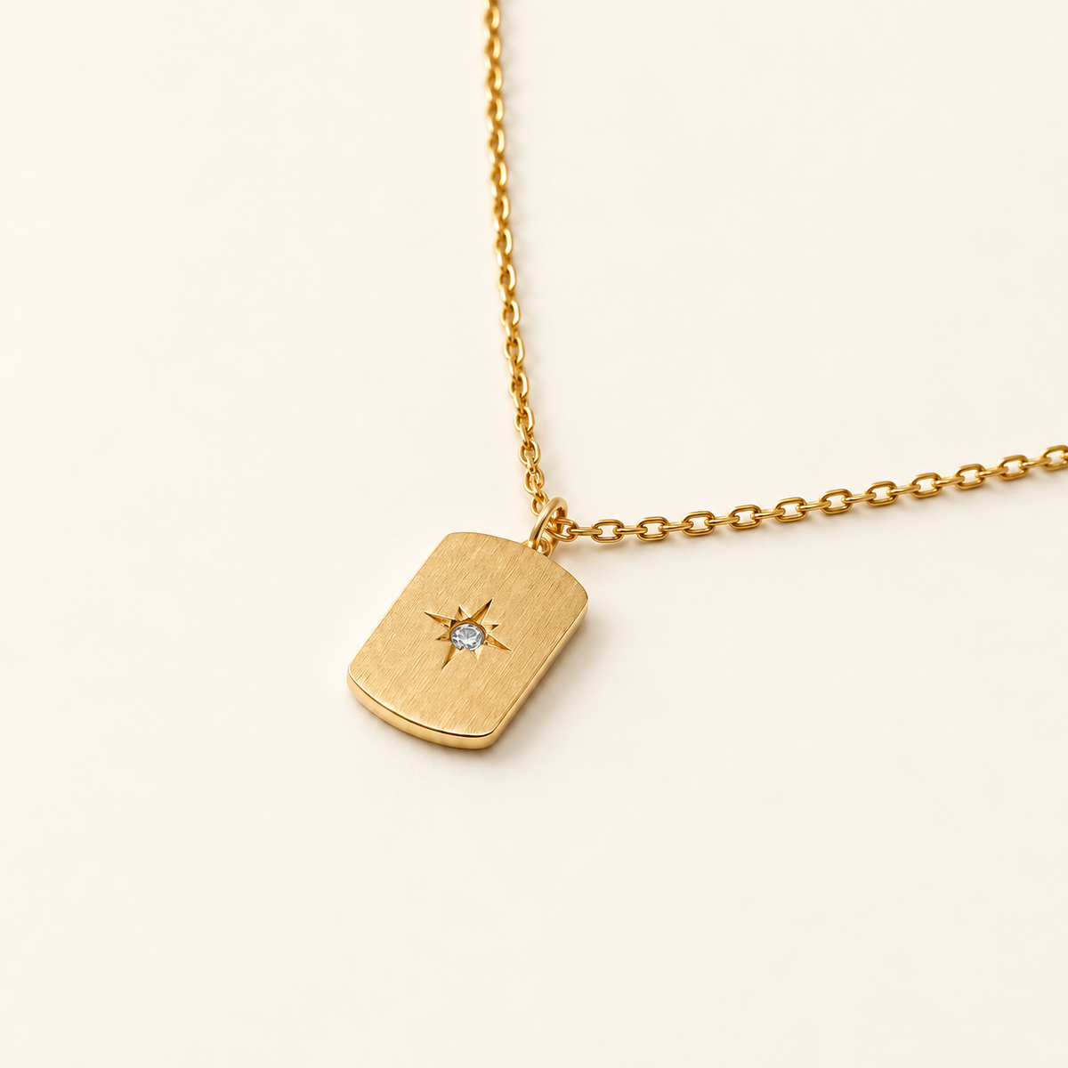 Stella Pendant Necklace in gold: brushed rectangular tag with a star-set stone on a fine cable chain, close-up on ivory.