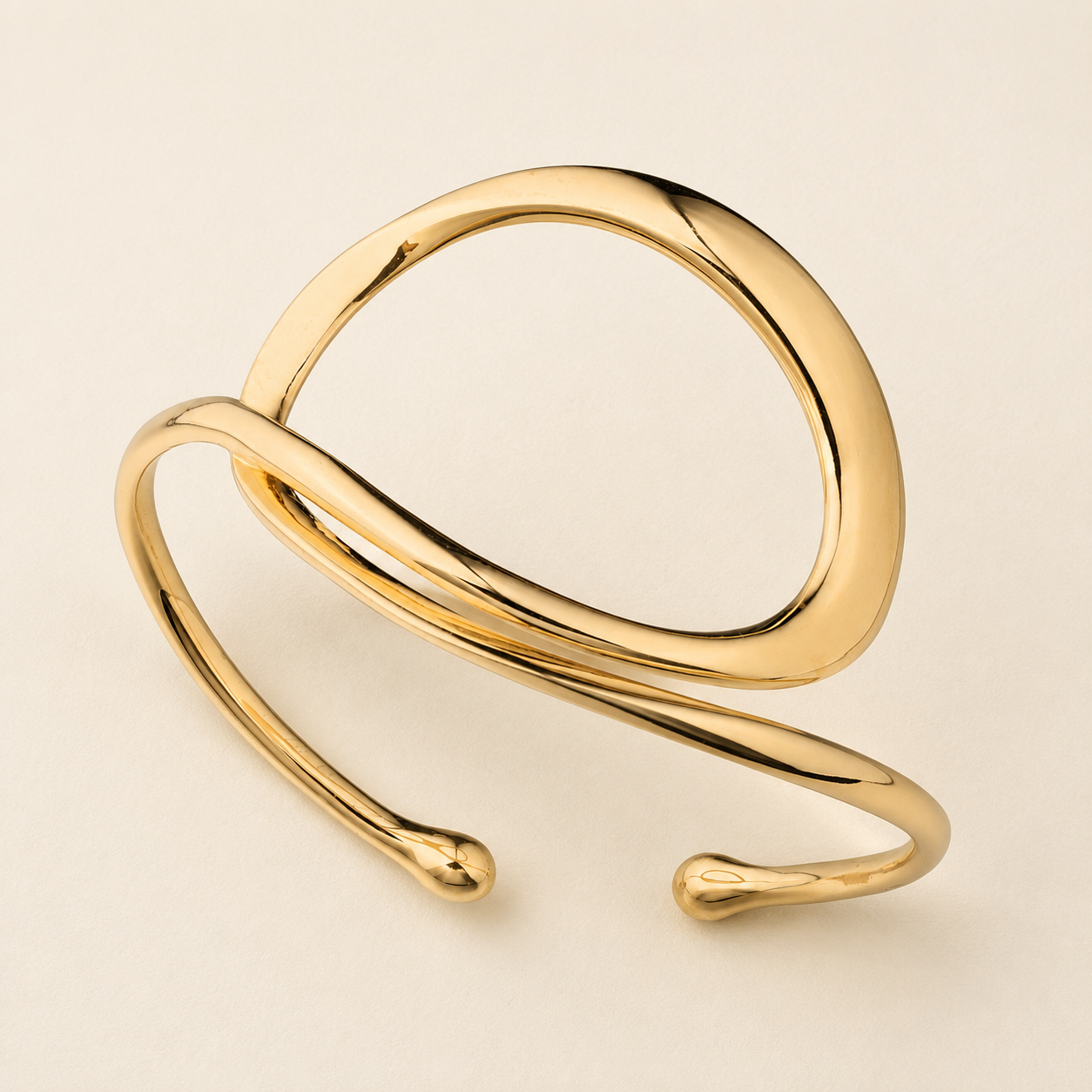 A polished gold open cuff bracelet with a modern, organic wavy design, photographed on a clean, solid light beige background.