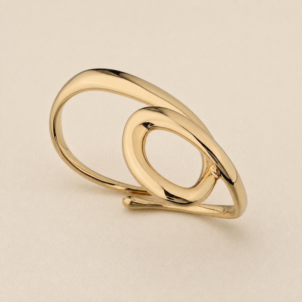 A polished gold-toned ring with an abstract, intertwined looped design, photographed on a clean, light beige textured background.