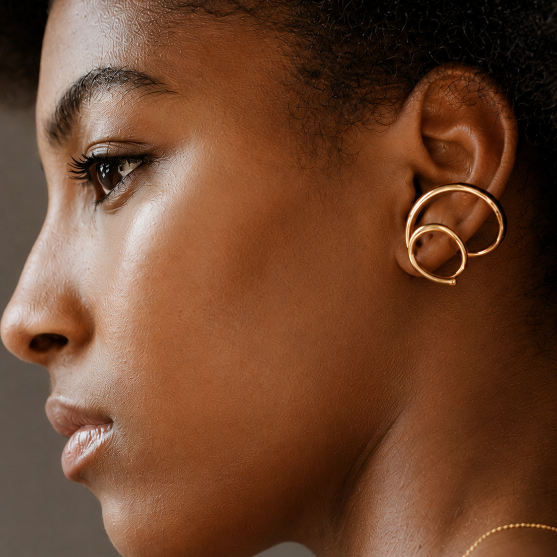 A close-up side profile of a woman wearing a pair of gold hoop earrings with a double-loop design.